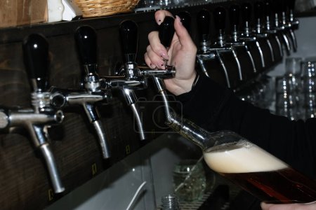 Foto de Detrás del mostrador. Las manos de las mujeres hermosamente y vierten fácilmente la cerveza en una botella. - Imagen libre de derechos