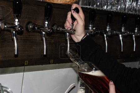 Foto de Detrás del mostrador. Las manos de las mujeres hermosamente y vierten fácilmente la cerveza en una botella. - Imagen libre de derechos