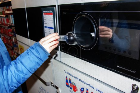 Foto de Nitra, Eslovaquia - 01.16.2024: Primer plano de la mano de un hombre poniendo una botella en una máquina de reciclaje de residuos. - Imagen libre de derechos