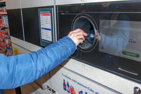 Foto de Nitra, Eslovaquia - 01.16.2024: Primer plano de la mano de un hombre poniendo una botella en una máquina de reciclaje de residuos. - Imagen libre de derechos