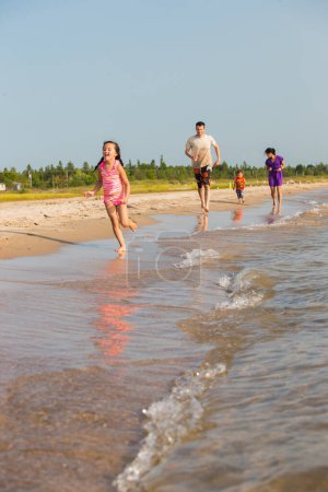 Téléchargez les photos : Happy Mixed Race Famille de quatre personnes Jouer et s'amuser sur la plage - en image libre de droit