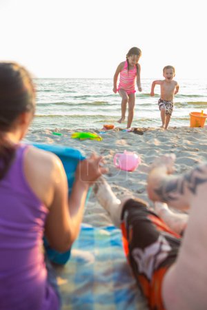 Téléchargez les photos : Happy Mixed Race Famille de quatre personnes Jouer et s'amuser sur la plage - en image libre de droit