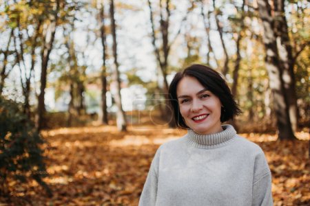 Photo for Happy smiling woman in park on sunny autumn day. Cheerful beautiful female in grey sweater on beautiful fall day. Natural light. High quality photo. - Royalty Free Image