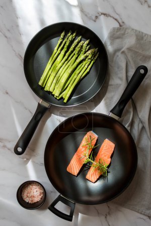 two frying pans studio product photography with asparagus and salmon. Food cooking background. Fresh asparagus in a pan on a marble background. The concept of healthy eating and diet. Top view. 