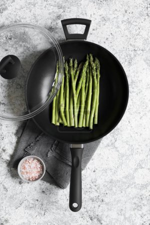 Frying pan with a lid product photography. Food cooking background. Fresh asparagus in a pan on a marble background. The concept of healthy eating and diet. Top view. 