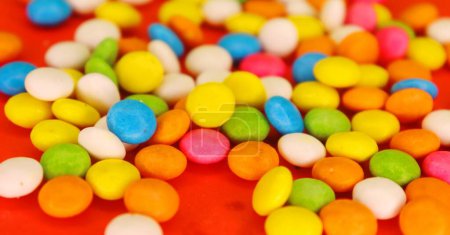 Téléchargez les photos : Petites pierres précieuses colorées Cadbury sur le fond rouge - en image libre de droit