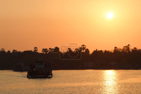 Foto de Barco de pasajeros flotando en el río al atardecer con fondo de cielo naranja - Imagen libre de derechos