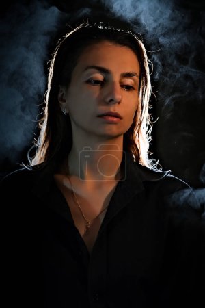 Téléchargez les photos : Silhouette d'une fille dans le noir. fumée. vapeur. fille dans une chambre sombre. - en image libre de droit