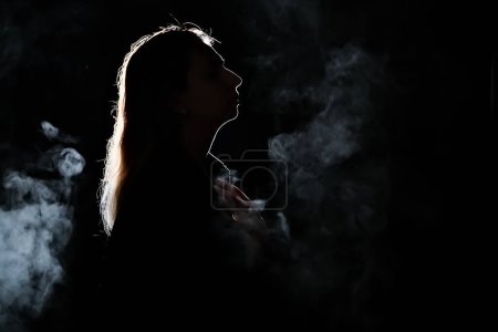 Téléchargez les photos : Silhouette d'une fille dans le noir. fumée. vapeur. fille dans une chambre sombre. - en image libre de droit
