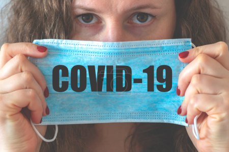 Foto de Una mujer sostiene una máscara facial. Inscripción en la máscara COVID-19. Pandemia conceptual, coronavirus, gripe. Mujer máscara de virus. protección facial en la prevención del coronavirus. - Imagen libre de derechos