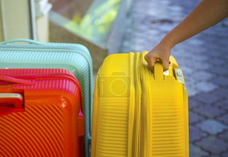 hand holds a suitcase for the handle. Bags for a trip. Colored Bags. Concept moving, travel, trip, flight. Concept Summer rest, holidays. Choosing a suitcase for travel. Hand take luggage carrier