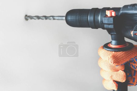 Photo for Workman hand with a rotary hammer. Hands in protective gloves with hammer drill perforator. close-up - Royalty Free Image