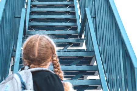 Photo for Schoolgirl looking up the stairs.. Concept  school days, start date, next stage, career ladder, the beginning of the way. girl in a uniform with a backpack. Girl near the stairs. - Royalty Free Image