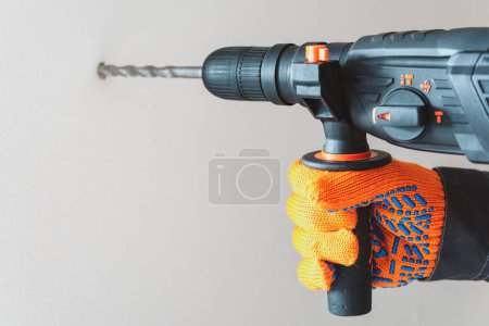  workman hand with a rotary hammer. Hands in protective gloves with hammer drill perforator. close-up