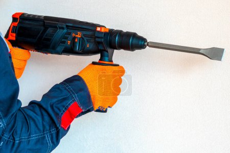  workman with a rotary hammer. Hands in protective gloves with hammer drill perforator. Copy space.
