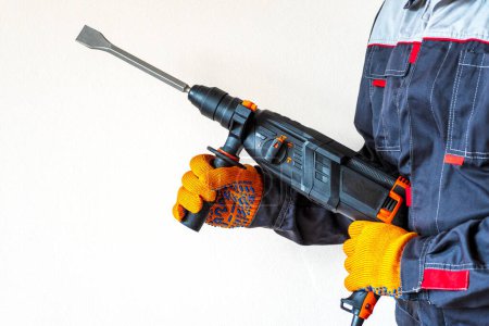  workman with a rotary hammer. Hands in protective gloves with hammer drill perforator. Copy space.