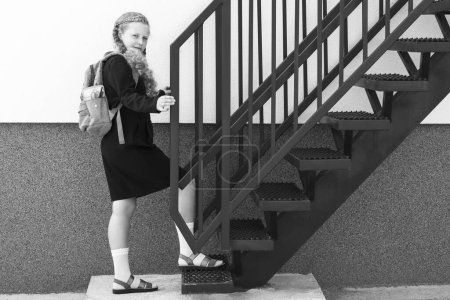 Schoolgirl with a smile climbs the stairs. Concept  school days, start date, next stage, career ladder, the beginning of the way. girl in a uniform with a backpack. Black and white photo