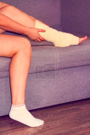  Woman with broken leg. female bandaging foot on the floor. The concept of a sore person with a limb injury. Close-up.