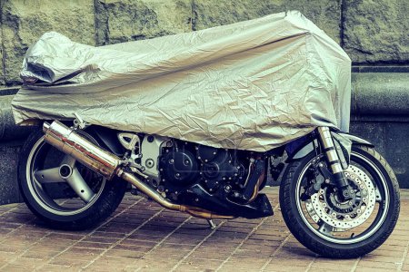 Abgedecktes Motorrad. Geparktes Motorrad in einer Schutzplane, Koffer. Das Motorrad war vom Regen mit einem Öltuch bedeckt. Wasserdichtes Parken im Freien während der Fahrt. 