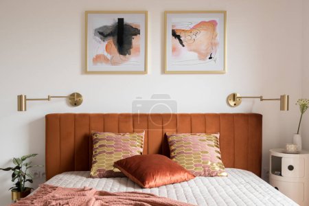 Photo for Elegant bedroom with art, golden lamps and stylish bed with velvet, ocher colored headboard - Royalty Free Image