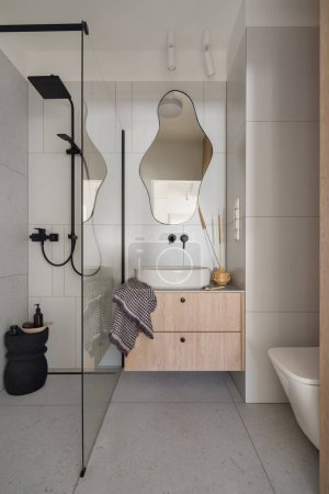 Téléchargez les photos : Simple gray tiles and modern design in bathroom with shower with black faucet and stylish mirror above washbasin - en image libre de droit