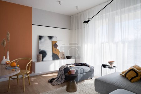 Photo for Bright and trendy living room with orange wall, art, modern furniture and big window behind white curtains - Royalty Free Image