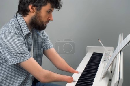 Téléchargez les photos : Brunet homme aux deux mains amputées joue du piano. La vie du gars personne musicien avec des handicaps physiques. Compositeur essaie de continuer à jouer et à créer de la musique après une blessure et d'écrire des notes. - en image libre de droit