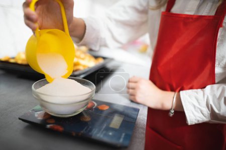 Foto de El cocinero vierte azúcar en un tazón en las escamas - Imagen libre de derechos