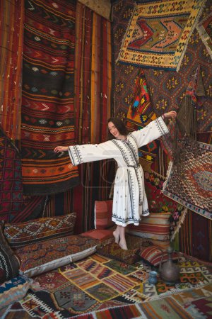 beautiful girl in a white dress with a teapot in a traditional turkish interior with many carpets on the wall