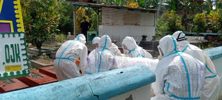 Foto de Klaten, Indonesia Enero-20, 2022: trabajadores de la salud vestidos con trajes PPE llevan un cuerpo cubierto de una víctima que murió de la enfermedad de covid-19 enterrada en un cementerio como lugar designado para el cadáver - Imagen libre de derechos