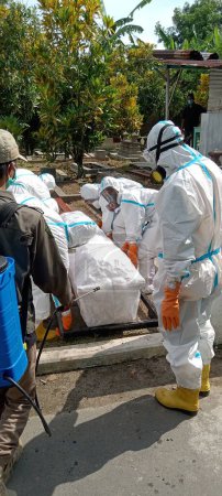 Foto de Klaten, Indonesia Enero-20, 2022: trabajadores de la salud vestidos con trajes PPE llevan un cuerpo cubierto de una víctima que murió de la enfermedad de covid-19 enterrada en un cementerio como lugar designado para el cadáver - Imagen libre de derechos