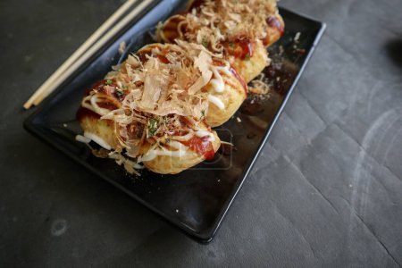 Photo for Takoyaki is a Japanese food, made from wheat flour dough, octopus meat, or other fillings, served with sauce, mayonnaise and topping in the form of katsuobushi or wood fish shavings. - Royalty Free Image