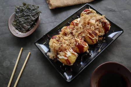 Téléchargez les photos : Takoyaki est un aliment japonais, fabriqué à partir de pâte de farine de blé, de viande de poulpe ou d'autres garnitures, servi avec de la sauce, de la mayonnaise et de la garniture sous forme de copeaux de katsuobushi ou de poisson de bois. - en image libre de droit