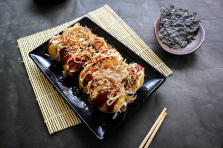 Photo for Takoyaki is a Japanese food, made from wheat flour dough, octopus meat, or other fillings, served with sauce, mayonnaise and topping in the form of katsuobushi or wood fish shavings. - Royalty Free Image