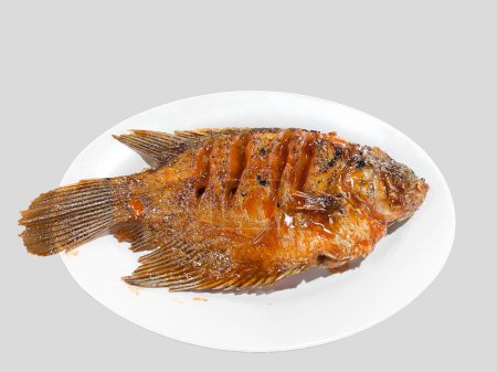 Grilled gourami or Gurame bakar with red barbeque sauce, vegetables, and chilli sauce on a white plated isolated on white background