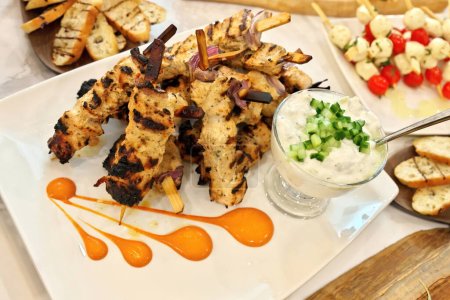 Foto de Vista en ángulo alto de brochetas de souvlaki de pollo griego a la parrilla o kebabs apilados en un plato blanco con un tazón de salsa tzatziki - Imagen libre de derechos