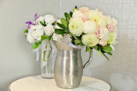 Photo for Beautiful Wedding Bouquets in Pitchers of Water on End Table Indoors. High quality photo - Royalty Free Image