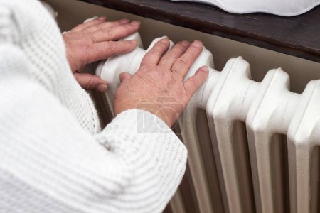 Foto de Senior woman is getting her hands warm on central heating system - Imagen libre de derechos