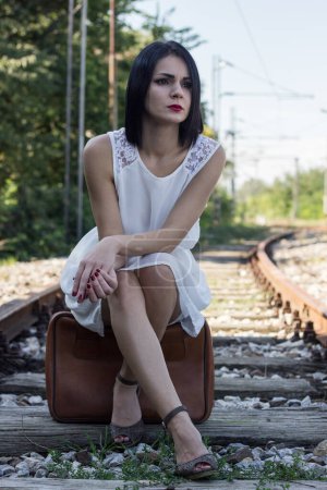 Téléchargez les photos : Beautiful woman sitting on a suitcase and waiting for the train - en image libre de droit
