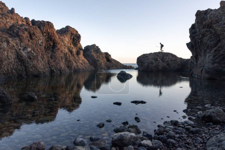 Photo for A fisherman walks along the rocks of a natural pool in Tenerife at dawn. High quality photo - Royalty Free Image