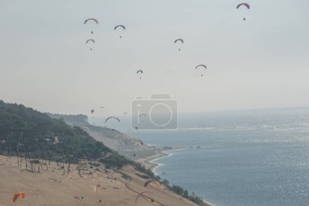 Téléchargez les photos : De nombreux parapentistes volant dans l'air venteux au-dessus de la dune de Pilat par une journée ensoleillée, Arcachon, Nouvelle-Aquitaine, France - en image libre de droit