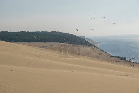 Téléchargez les photos : De nombreux parapentistes volant dans l'air venteux au-dessus de la dune de Pilat par une journée ensoleillée, Arcachon, Nouvelle-Aquitaine, France - en image libre de droit