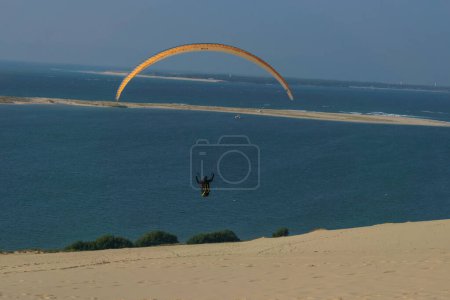 Téléchargez les photos : Parapente unique volant dans l'air venteux au-dessus de la dune de Pilat par une journée ensoleillée, Arcachon, Nouvelle-Aquitaine, France - en image libre de droit