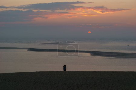 Téléchargez les photos : Silhouette de couple debout devant le coucher du soleil avec vue sur la mer à la Dune du Pilat, Arcachon, Nouvelle-Aquitaine, France - en image libre de droit