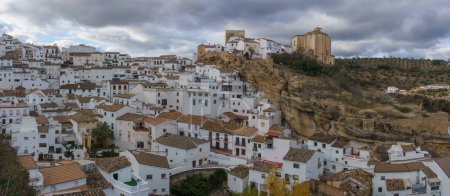 Blick auf ein typisch andalusisches Dorf mit weißen Häusern und Straße mit in Felsüberhänge eingebauten Wohnhäusern, Setenil de las Bodegas, Andalusien, Spanien