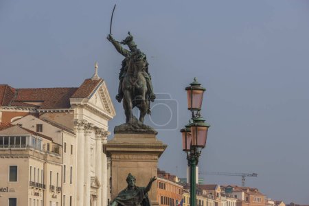 Bronze statue of Monument of Vittorio Emanuele II on Riva degli Schiavoni and a street lantern in foreground, Venice, Veneto, Italy