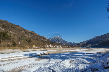 Lago embalse congelado vacío durante el invierno con pueblo en el paisaje montañoso de los Alpes, Barcis, Friuli-Venezia Giulia, Italia