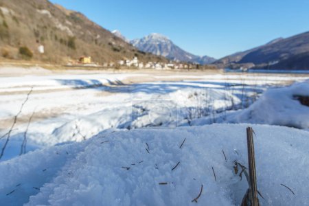Close up of the shore of empty frozen reservoir lake during winter in the mountain landscape of the Alps, Barcis, Friuli-Venezia Giulia, Italy