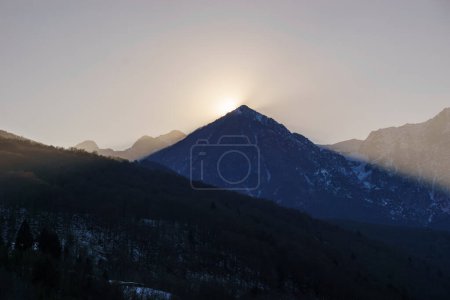 Sol de invierno detrás de un pico de montaña de un paisaje alpino de invierno en Barcis, Friuli-Venezia Giulia, Italia
