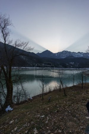 Puesta de sol de invierno detrás de un pico de montaña de un paisaje alpino de invierno con lago embalse en Barcis, Friuli-Venezia Giulia, Italia